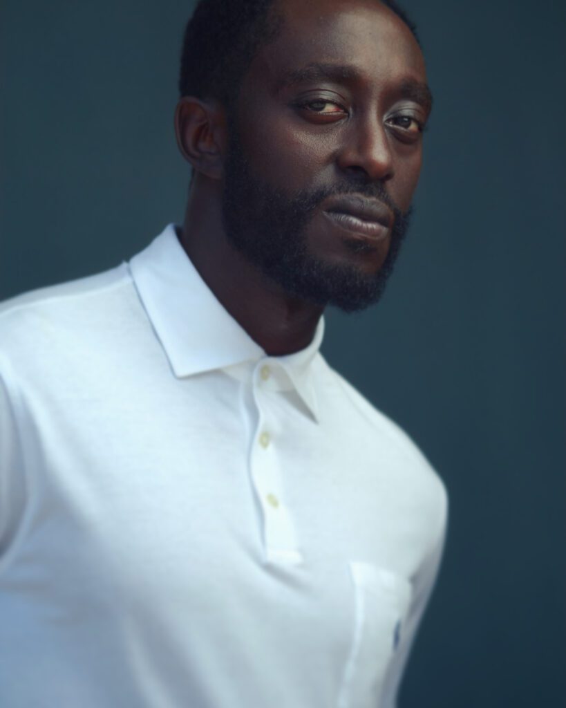 a black man in a white teeshirt against a blue wall