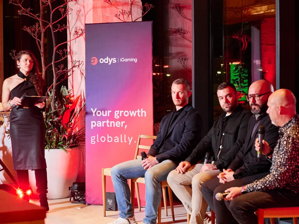 Candid shot of a conversation, with one participant turning to look at the camera with an engaged expression at the Odys panel talk