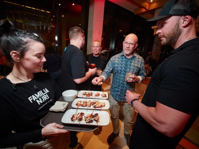 Small group portrait of Odys clients enjoying cocktails, and food with a mix of candid interaction and direct engagement with the corporate event photographer.