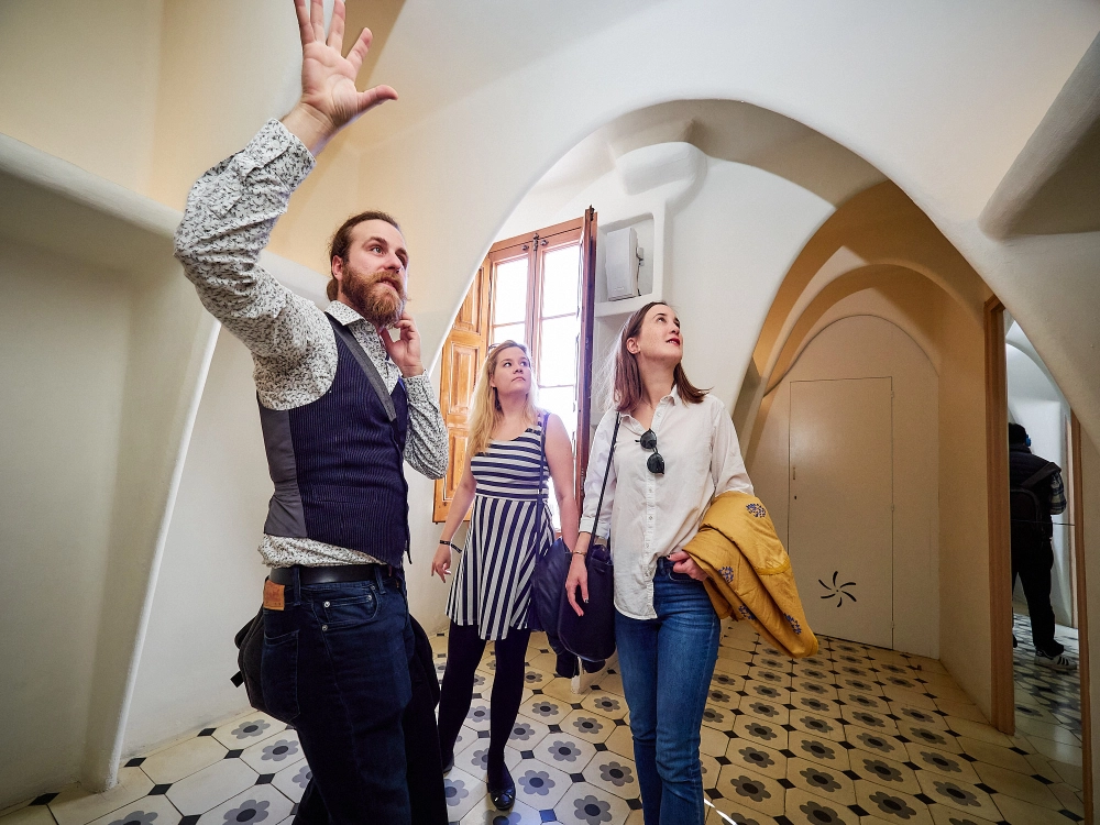 A tour group walks through a white, minimalist attic space lined with a series of repeating, rib-like arched structures.