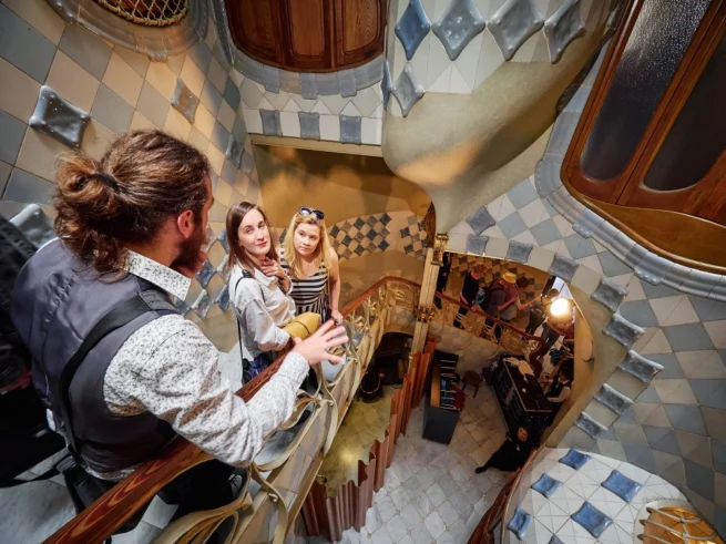 A tour group peers over a railing into a tall, tiled courtyard filled with shades of blue tiles that simulate an underwater effect.