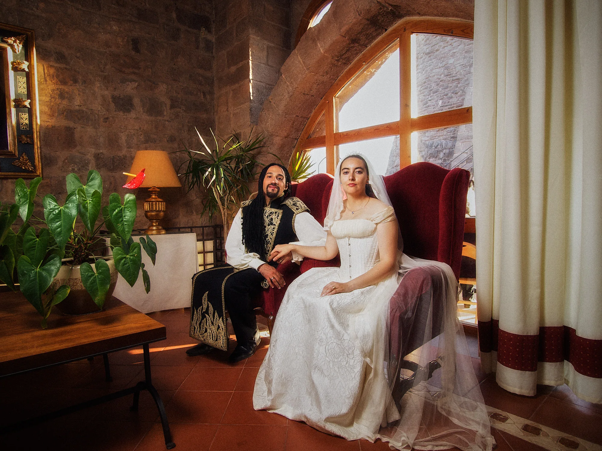 Emily and Regis seated in a historic room at Parador de Cardona wearing neo-Gothic wedding attire